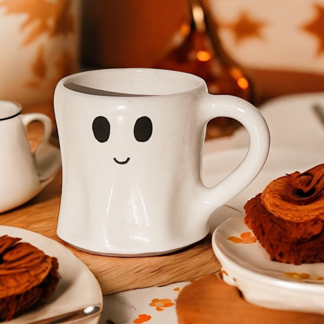Ghost-shaped mug on a table with pastries and a cozy background