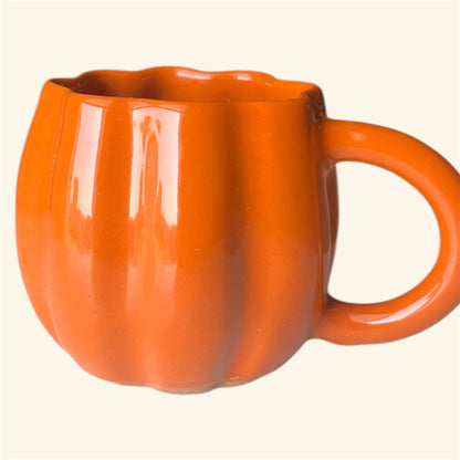 Close-up of orange pumpkin-shaped ceramic mug on light background